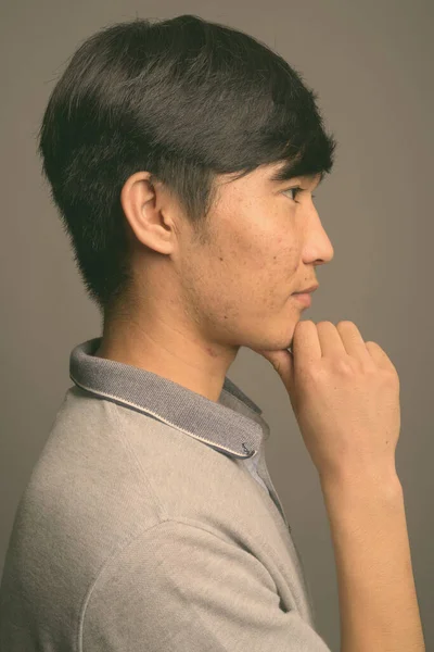 Gri arka planda gri polo tişört giyen genç Asyalı adam. — Stok fotoğraf