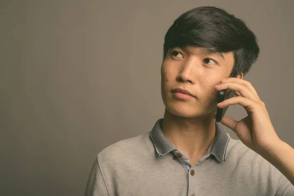 Jeune homme asiatique en utilisant un téléphone mobile sur fond gris — Photo
