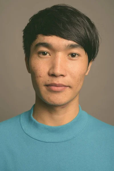 Ung asiatisk man bär blå tröja mot grå bakgrund — Stockfoto