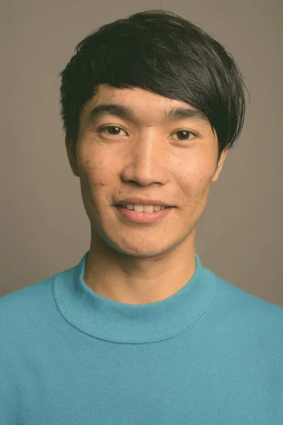 파란 스웨터를 입고 잿빛 배경에 반한 아시아 청년 — 스톡 사진