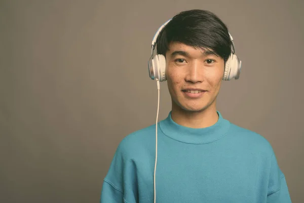 Молодий азіат слухає музику на сірому фоні — стокове фото