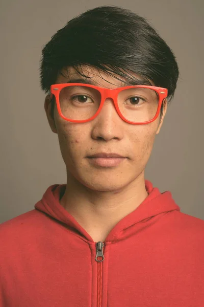 Молодий азіатський чоловік у червоній куртці з окулярами на сірому тлі — стокове фото