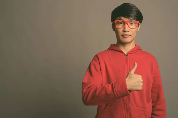 Młody Azjata w czerwonej kurtce z okularami na szarym tle — Zdjęcie stockowe