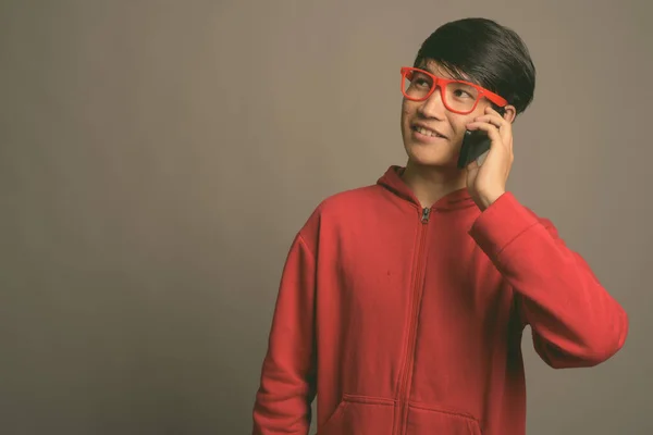 Giovane uomo asiatico indossa giacca rossa con occhiali contro sfondo grigio — Foto Stock