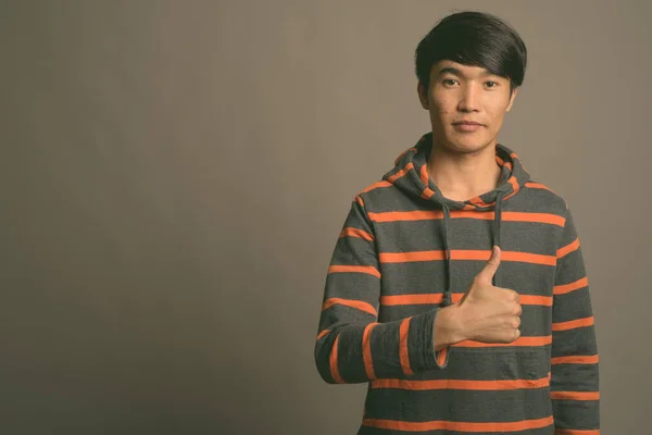 Ung asiatisk man bär randig hoodie mot grå bakgrund — Stockfoto