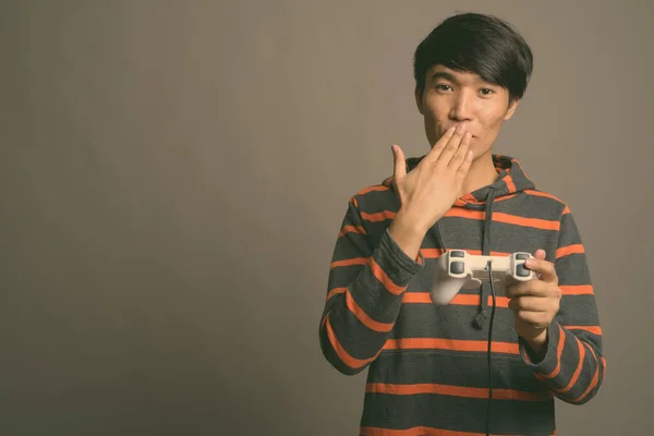 Jovem homem asiático jogando jogos contra fundo cinza — Fotografia de Stock