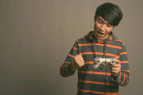 若いアジアの男は灰色の背景に対してゲームをプレイ — ストック写真