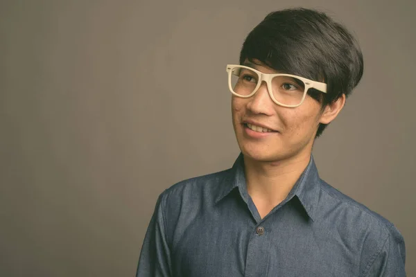 Genç Asyalı gözlüklü adam gri arka planda zeki görünüyor. — Stok fotoğraf