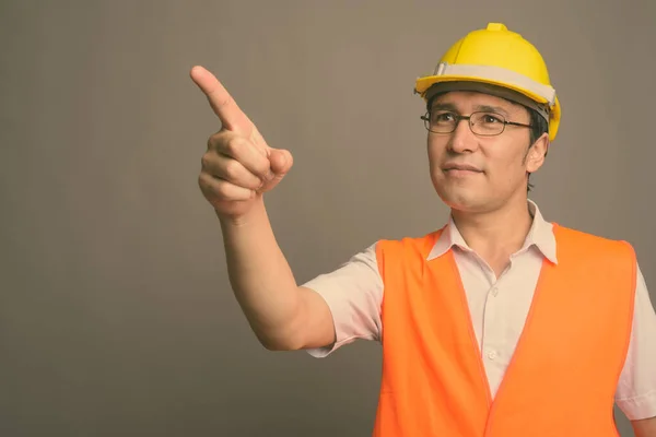 Joven hombre asiático trabajador de la construcción con anteojos sobre fondo gris —  Fotos de Stock