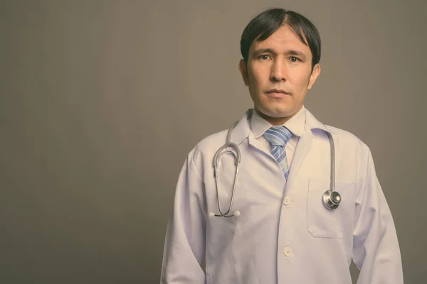 Young Asian man doctor against gray background — Stock Photo, Image