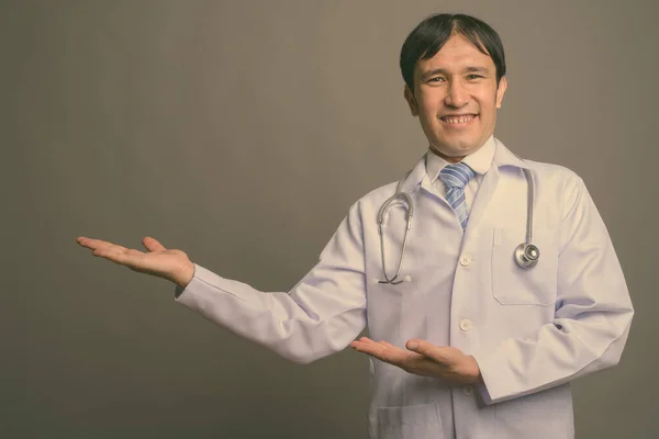 Junger asiatischer Arzt vor grauem Hintergrund — Stockfoto