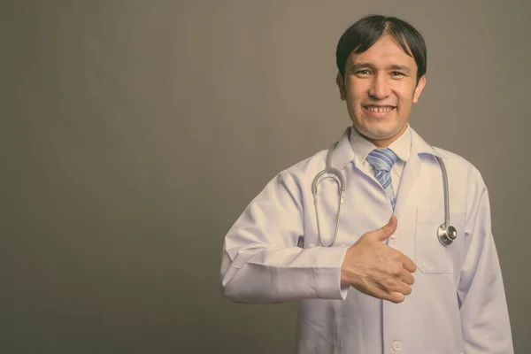 Mladý asijský muž lékař na šedém pozadí — Stock fotografie