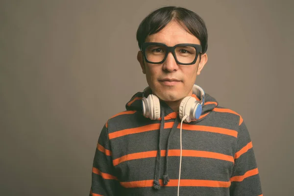 Młody Azji nerd człowiek w kapturze i słuchawki na szarym tle — Zdjęcie stockowe