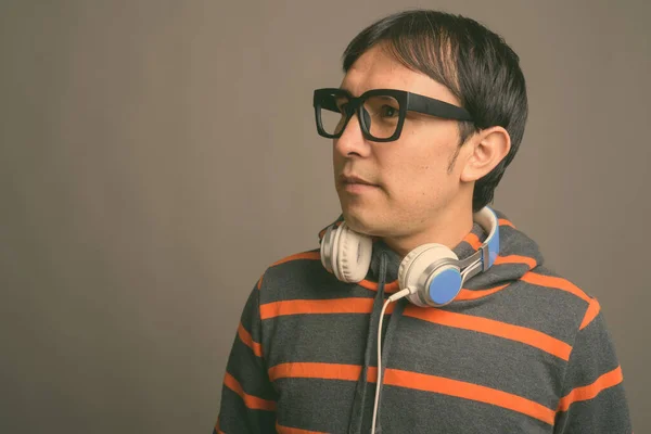 Joven asiático nerd hombre usando sudadera con capucha y auriculares contra fondo gris —  Fotos de Stock