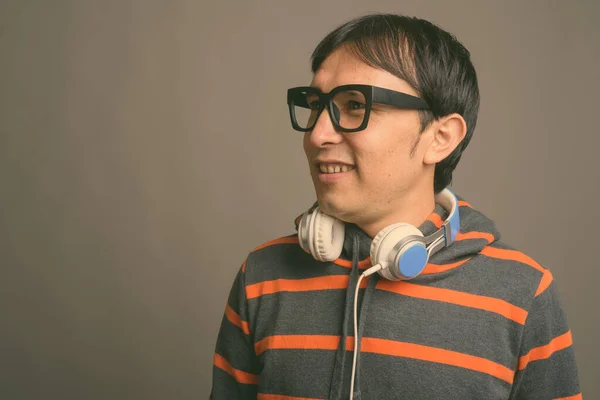 Young Asian nerd man wearing hoodie and headphones against gray background
