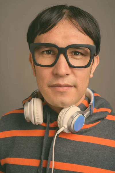 Ung asiatisk nörd man bär huvtröja och hörlurar mot grå bakgrund — Stockfoto