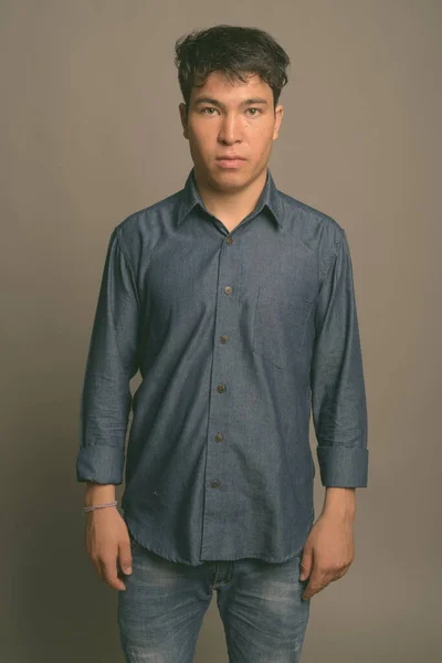 Mladý asijský muž v modré košili na šedém pozadí — Stock fotografie