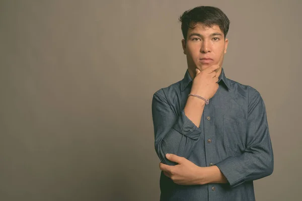 Ung asiatisk man bär blå skjorta mot grå bakgrund — Stockfoto