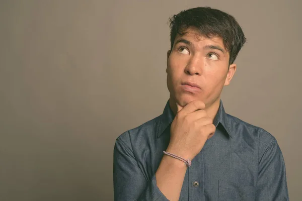 Mladý asijský muž v modré košili na šedém pozadí — Stock fotografie