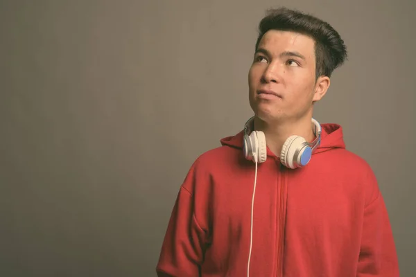 Joven asiático hombre usando auriculares contra fondo gris —  Fotos de Stock