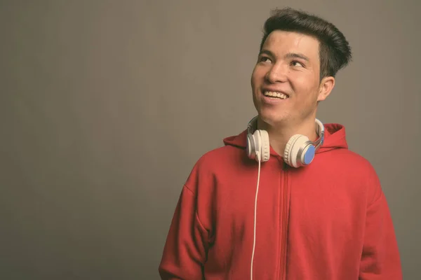 Joven asiático hombre usando auriculares contra fondo gris — Foto de Stock