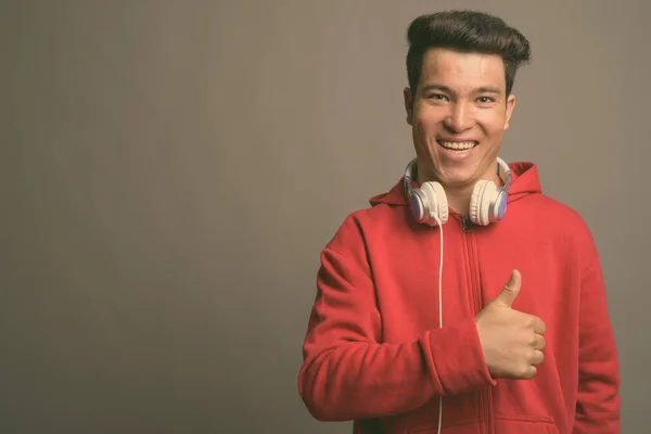 Joven asiático hombre usando auriculares contra fondo gris — Foto de Stock