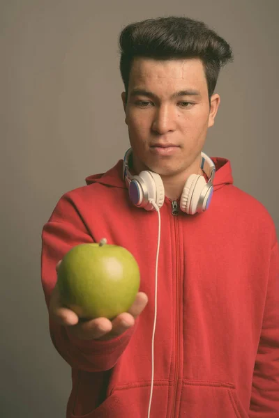 Jovem homem asiático usando fones de ouvido contra fundo cinza — Fotografia de Stock
