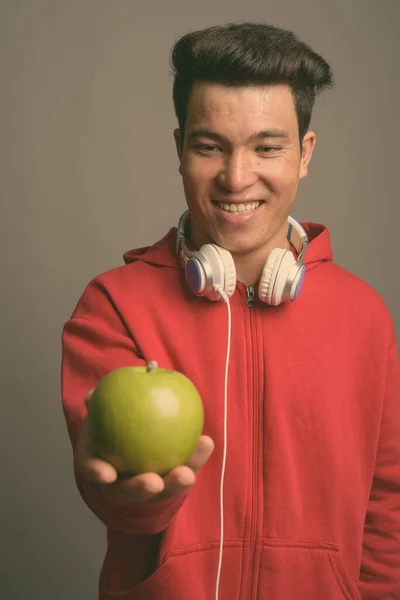 Mladý asijský muž nosí sluchátka na šedém pozadí — Stock fotografie