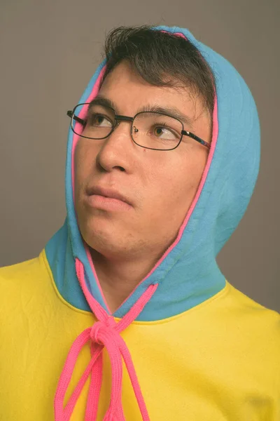 Jeune homme asiatique portant un sweat à capuche coloré et des lunettes sur fond gris — Photo