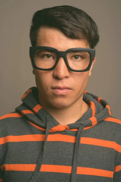 Joven asiático nerd hombre usando sudadera con capucha contra gris fondo — Foto de Stock