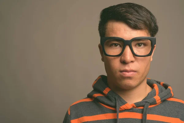Mladý asijský nerd muž nosí mikinu proti šedému pozadí — Stock fotografie