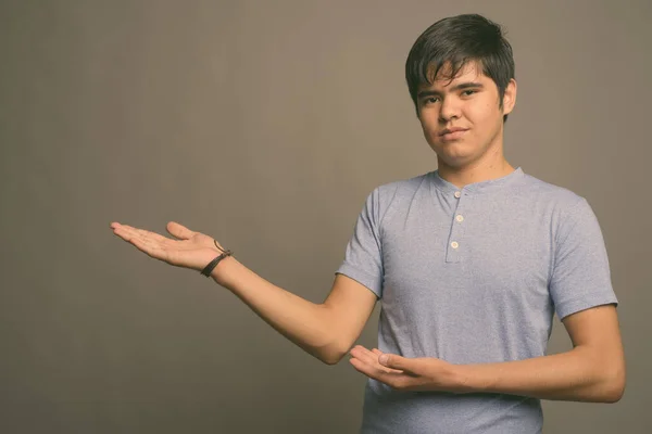 Junger asiatischer Teenager trägt blaues Hemd vor grauem Hintergrund — Stockfoto