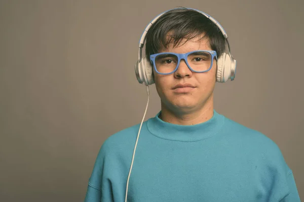 Jovem adolescente asiático ouvindo música contra fundo cinza — Fotografia de Stock