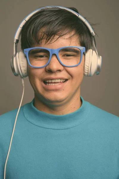 Jovem adolescente asiático ouvindo música contra fundo cinza — Fotografia de Stock