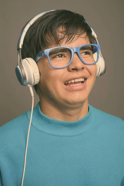 Jong aziatische tiener jongen luisteren naar muziek tegen grijs achtergrond — Stockfoto