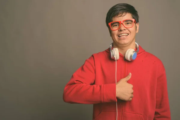 Jovem adolescente asiático usando fones de ouvido contra fundo cinza — Fotografia de Stock