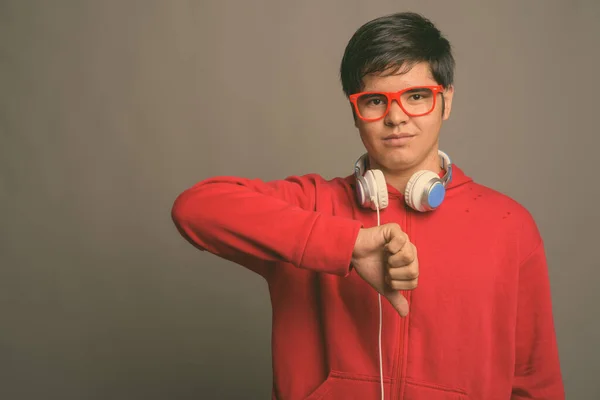 Młody Azji nastolatek chłopiec noszenie słuchawki na szarym tle — Zdjęcie stockowe