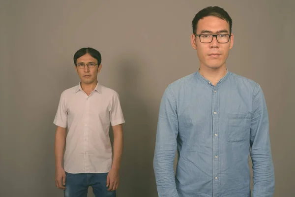 Két fiatal ázsiai üzletember szemüveget visel, szürke háttér mellett. — Stock Fotó