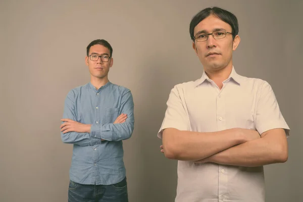 Dwóch młodych azjatyckich biznesmenów w okularach na szarym tle — Zdjęcie stockowe