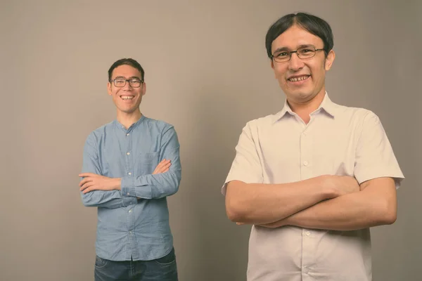 Two young Asian businessmen wearing eyeglasses together against gray background — Stock Photo, Image