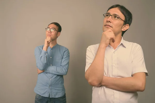 Dwóch młodych azjatyckich biznesmenów w okularach na szarym tle — Zdjęcie stockowe