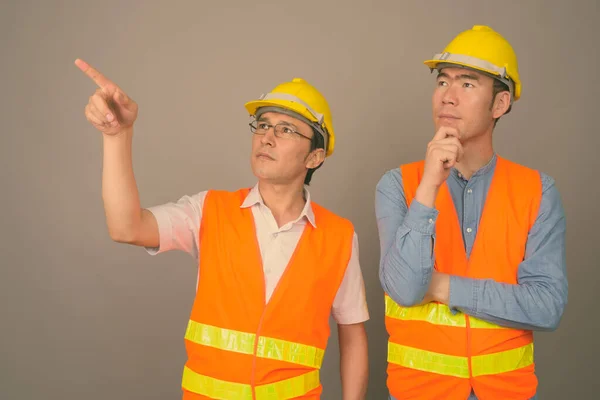 Dos jóvenes asiáticos trabajadores de la construcción juntos contra el fondo gris —  Fotos de Stock