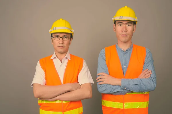 Dwóch młodych azjatyckich robotników budowlanych razem na szarym tle — Zdjęcie stockowe