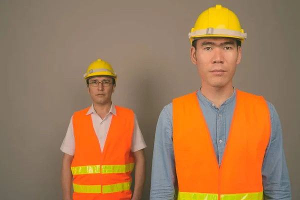 Dos jóvenes asiáticos trabajadores de la construcción juntos contra el fondo gris —  Fotos de Stock