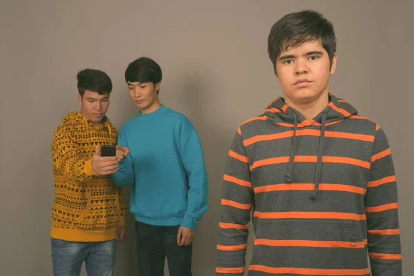 Tres jóvenes amigos asiáticos juntos contra fondo gris — Foto de Stock