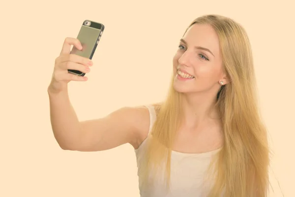 Estudio de disparo de la joven adolescente feliz sonriendo mientras toma foto selfie con teléfono móvil —  Fotos de Stock