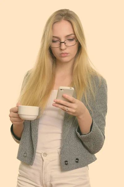 Young beautiful businesswoman using mobile phone while holding coffee cup — Stock Photo, Image