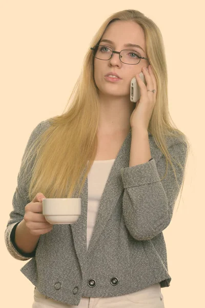 Cep telefonuyla konuşan ve elinde kahve fincanı tutan genç ve güzel bir iş kadını. — Stok fotoğraf