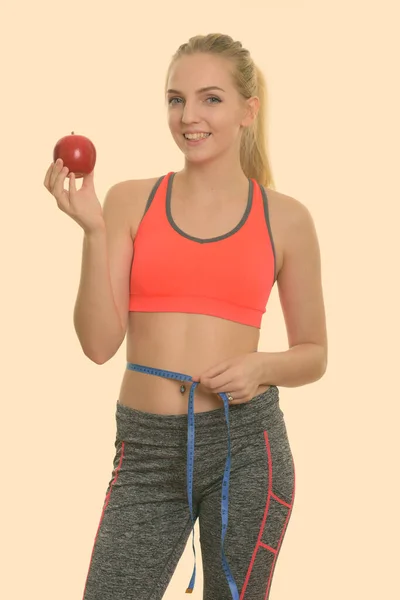 Joven adolescente feliz sonriendo mientras sostiene la manzana roja y mide la cintura listo para el gimnasio —  Fotos de Stock