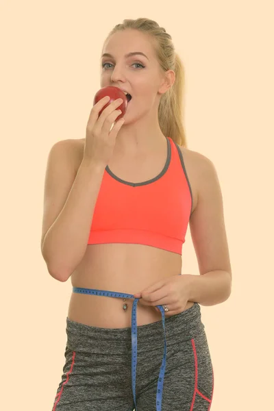 Stüdyoda genç ve güzel bir kızın kırmızı elma yiyip, belinin ölçüsünü aldığı bir fotoğraf. — Stok fotoğraf